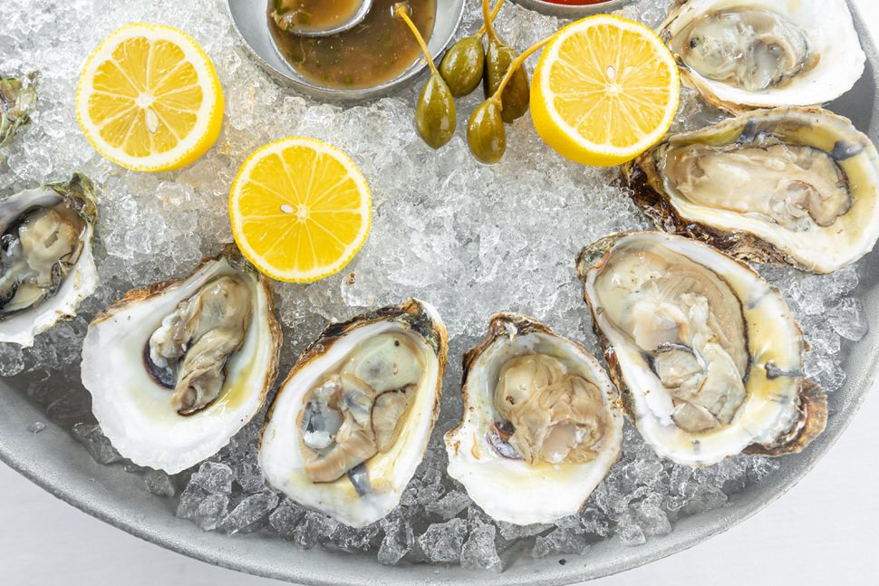 Fresh raw oysters on the half shell served over crushed ice with lemon halves, caperberries, and mignonette sauce on a chilled platter.