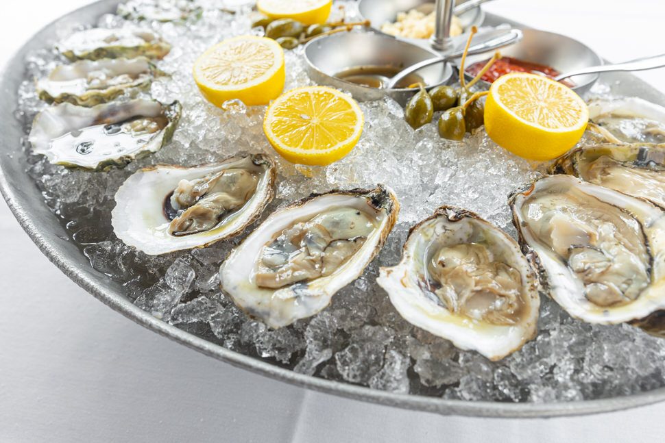 Freshly shucked oysters on the half shell arranged over crushed ice on a silver platter, garnished with halved lemons and small bowls of cocktail sauce and mignonette.