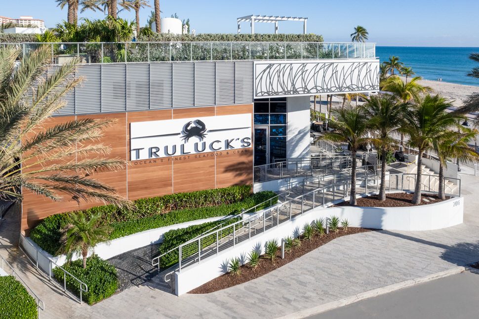 Exterior of Truluck’s Fort Lauderdale featuring the Ocean’s Finest Seafood & Crab signage on a wood-paneled facade, palm trees, elevated entrance ramp, and ocean views along the beachfront.