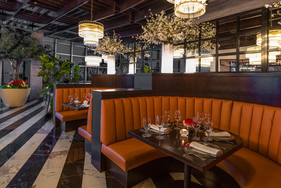 Elegant booth seating at Truluck’s Fort Lauderdale featuring warm leather banquettes, dark wood tables set with wine glasses and folded napkins, glowing chandeliers, and lush greenery in a refined dining room setting.