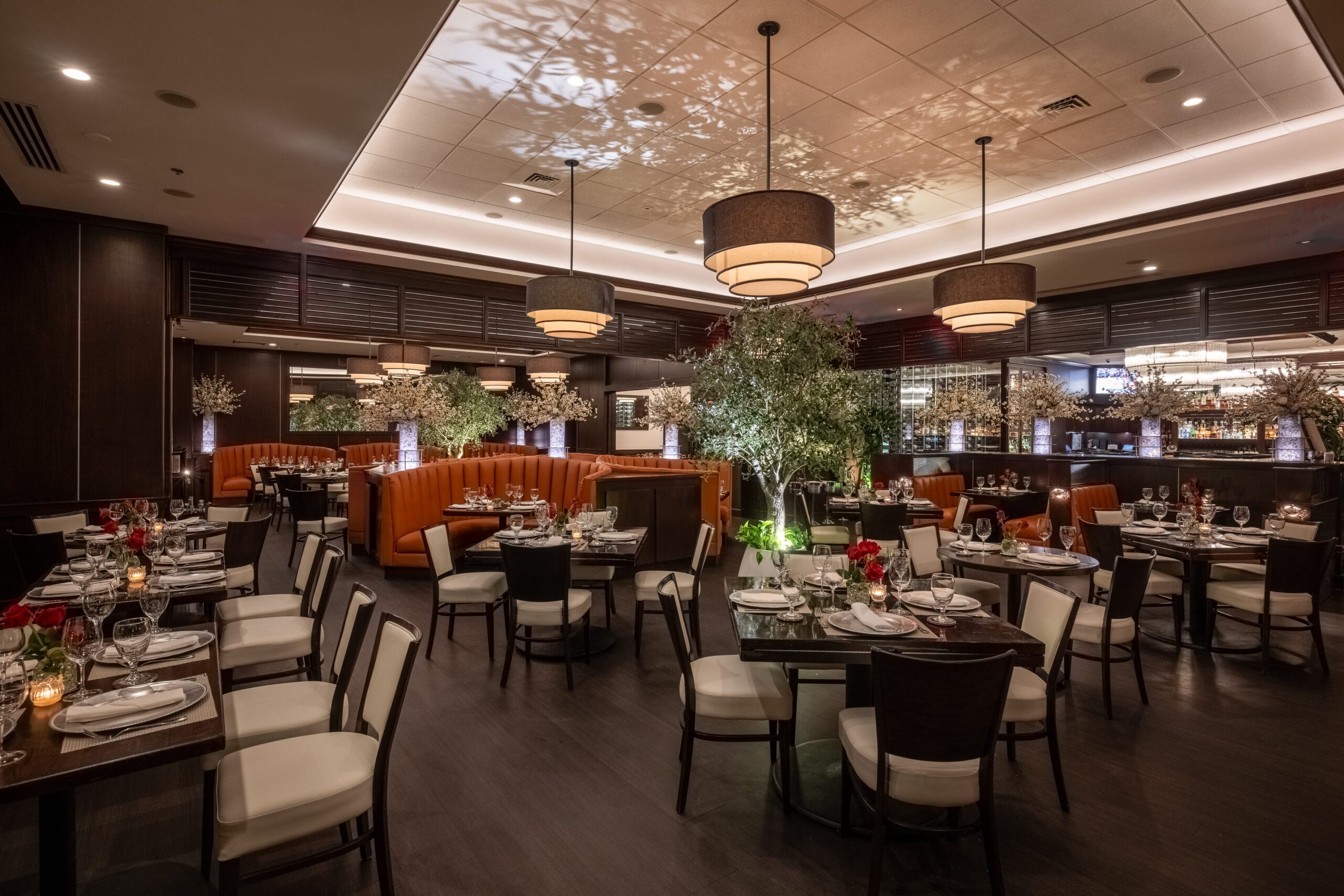 Truluck’s Miami dining room with curved leather banquettes, statement lighting, greenery accents, and refined table settings.