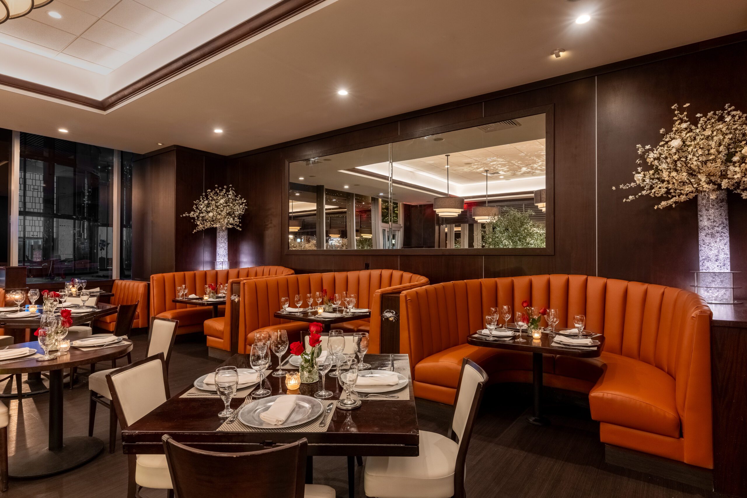 Curved banquette seating at Truluck’s Miami with elegantly set tables, crystal stemware, red rose accents, and floor-to-ceiling windows creating a refined dining atmosphere.