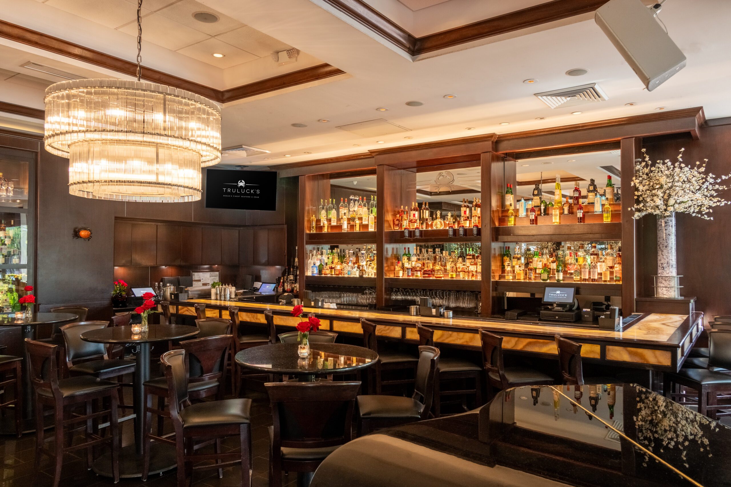 Elegant bar interior at Truluck’s Miami featuring a crystal chandelier, polished wood bar, premium spirits display, and intimate cocktail seating.