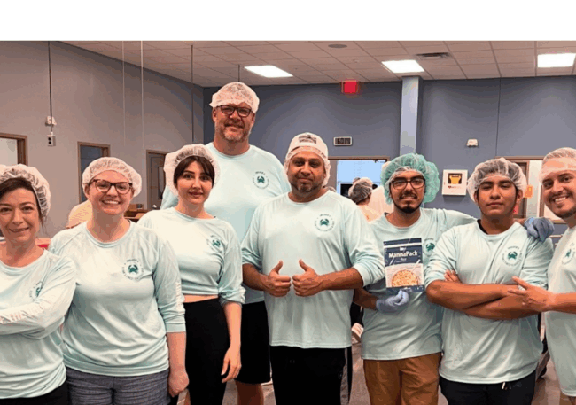 Truluck’s Rosemont team members wearing hairnets and light blue shirts volunteer together at a food bank, smiling while packaging meals.
