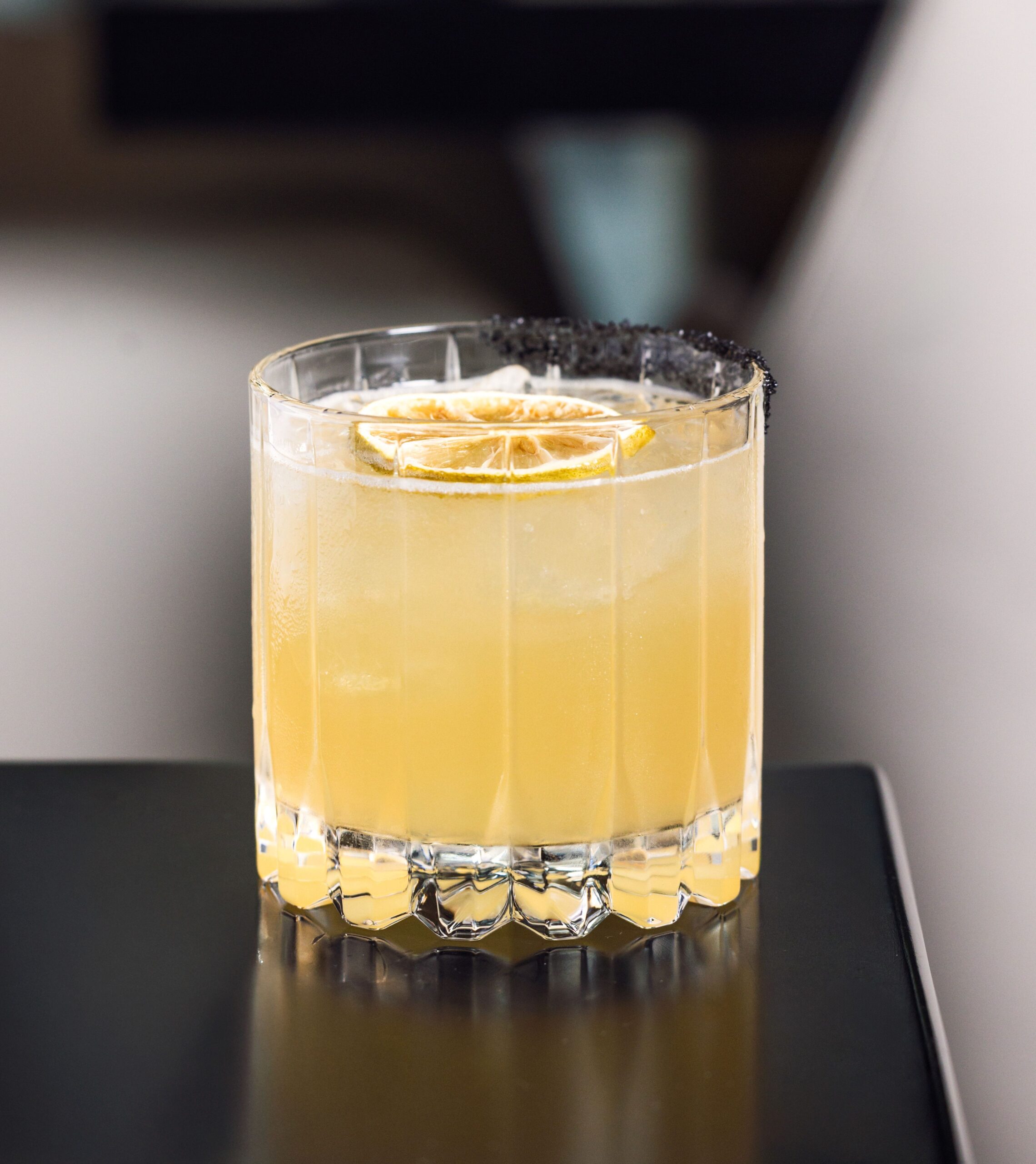 A refined El Tesoro reposado single-barrel margarita cocktail served on the rocks in a cut crystal glass with a dramatic black salt rim.