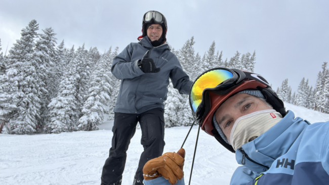 Mickey Gonzalez, General Manager of Truluck’s Miami, skiing on a snowy mountain with a friend, wearing winter gear and goggles, surrounded by snow-covered trees.