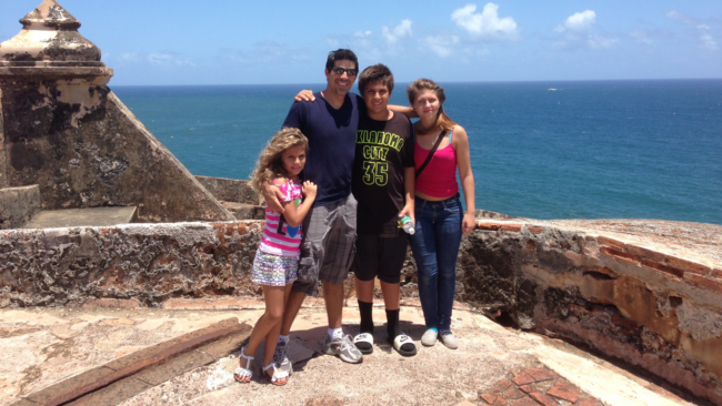 Mickey Gonzalez, General Manager of Truluck’s Miami, posing with family on a historic seaside overlook, with ocean views and blue skies in the background.