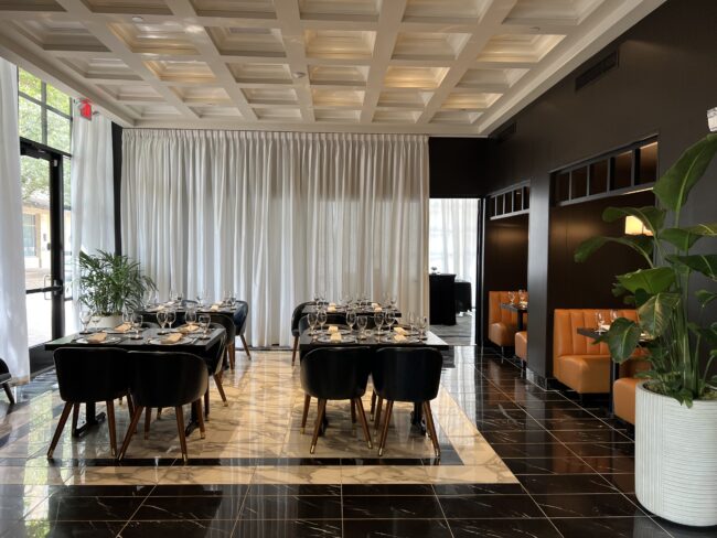 Truluck’s Plano private dining space at The Shops at Legacy, featuring a modern, elegant interior with marble floors, coffered ceiling, black tables set with fine glassware, and warm leather booths—ideal for group dining and special events.