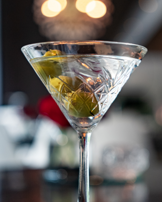 Close-up of a classic martini in a cut-crystal glass, garnished with olives and set against a softly lit Truluck’s dining room backdrop.