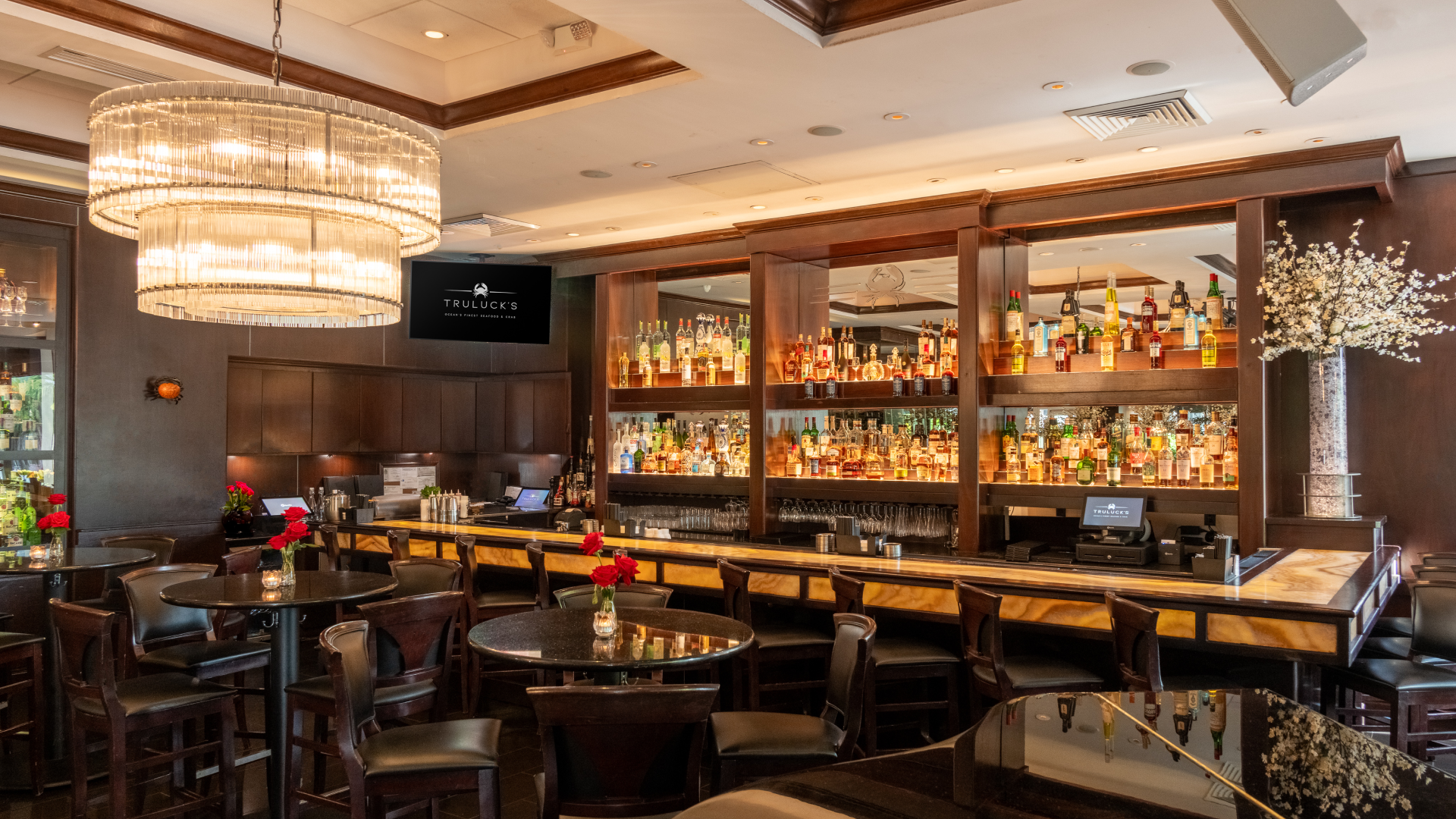 The bar at Truluck's, featuring an extensive whiskey and spirits selection, crystal chandelier, and intimate lounge seating for cocktails and Happy Hour during the World Cup