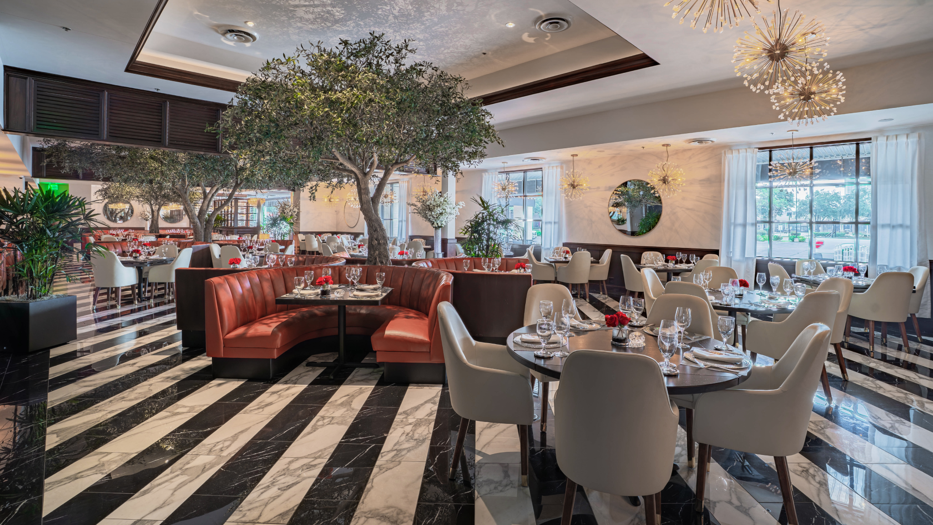 The renovated dining room at Truluck's Galleria in Houston, featuring floor-to-ceiling olive trees and marble flooring — the original Truluck's location founded in 1992 and the closest fine dining seafood restaurant to NRG Stadium