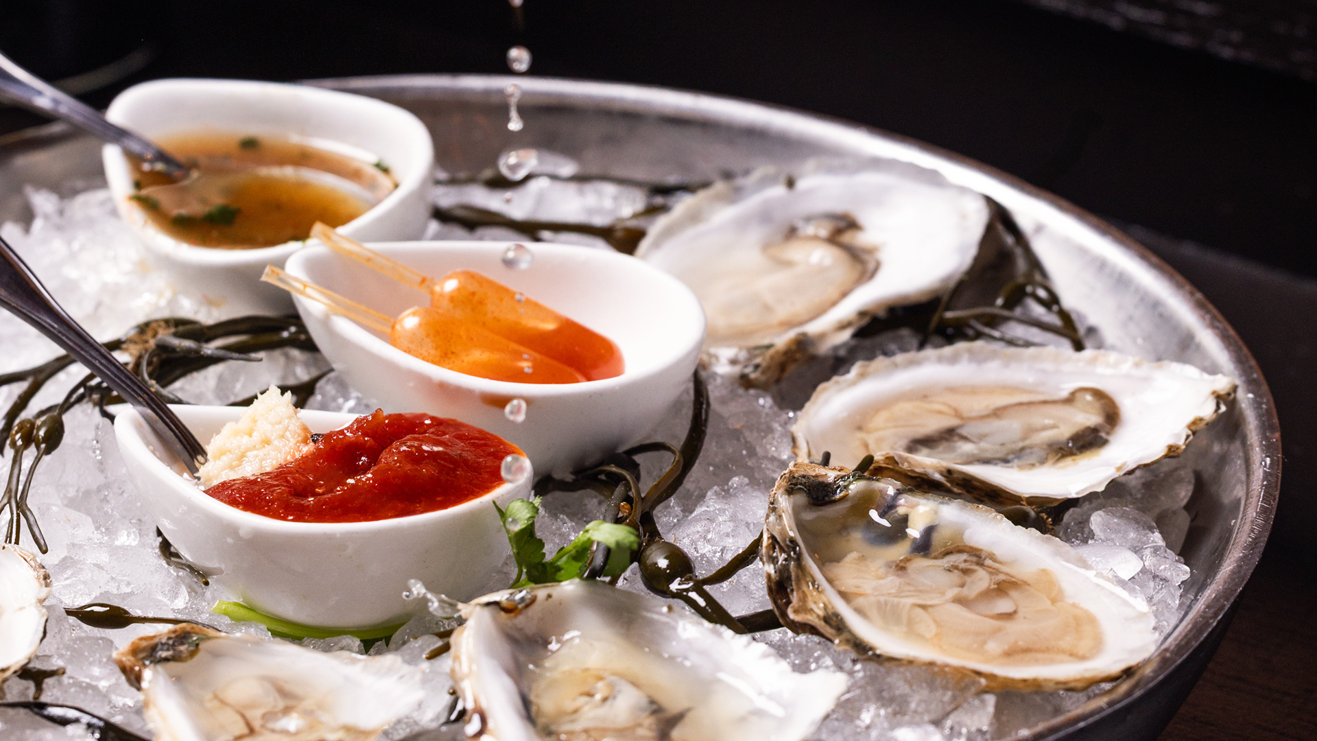Raw oysters on ice with cocktail sauce, horseradish, mignonette, and seafood garnishes served on a chilled platter.