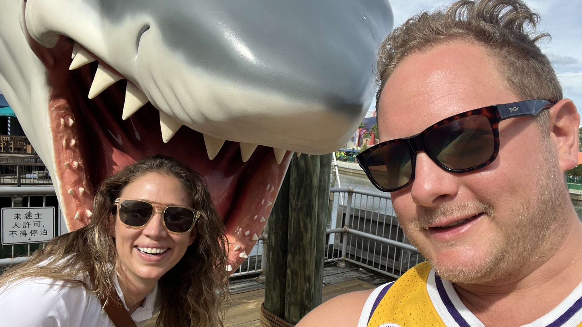 Johnny Griesedieck of Truluck’s Naples taking a selfie with a companion in front of a large shark display near the water.