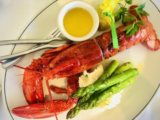 Steamed Maine lobster served with drawn butter, mashed potatoes, asparagus, lemon, and a fresh parsley garnish.