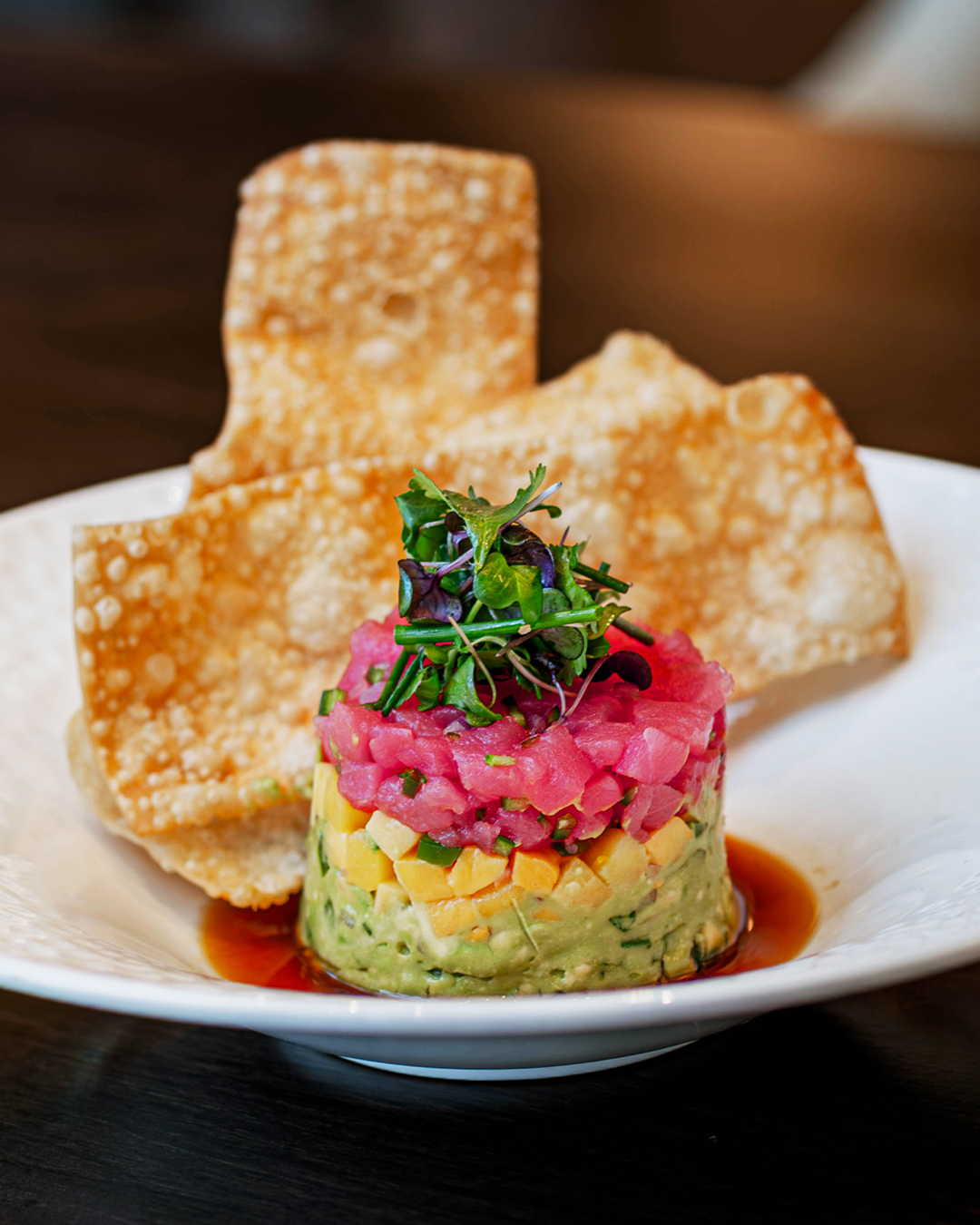 Ahi tuna tartare layered with avocado and mango, topped with microgreens and served with crispy wonton chips.