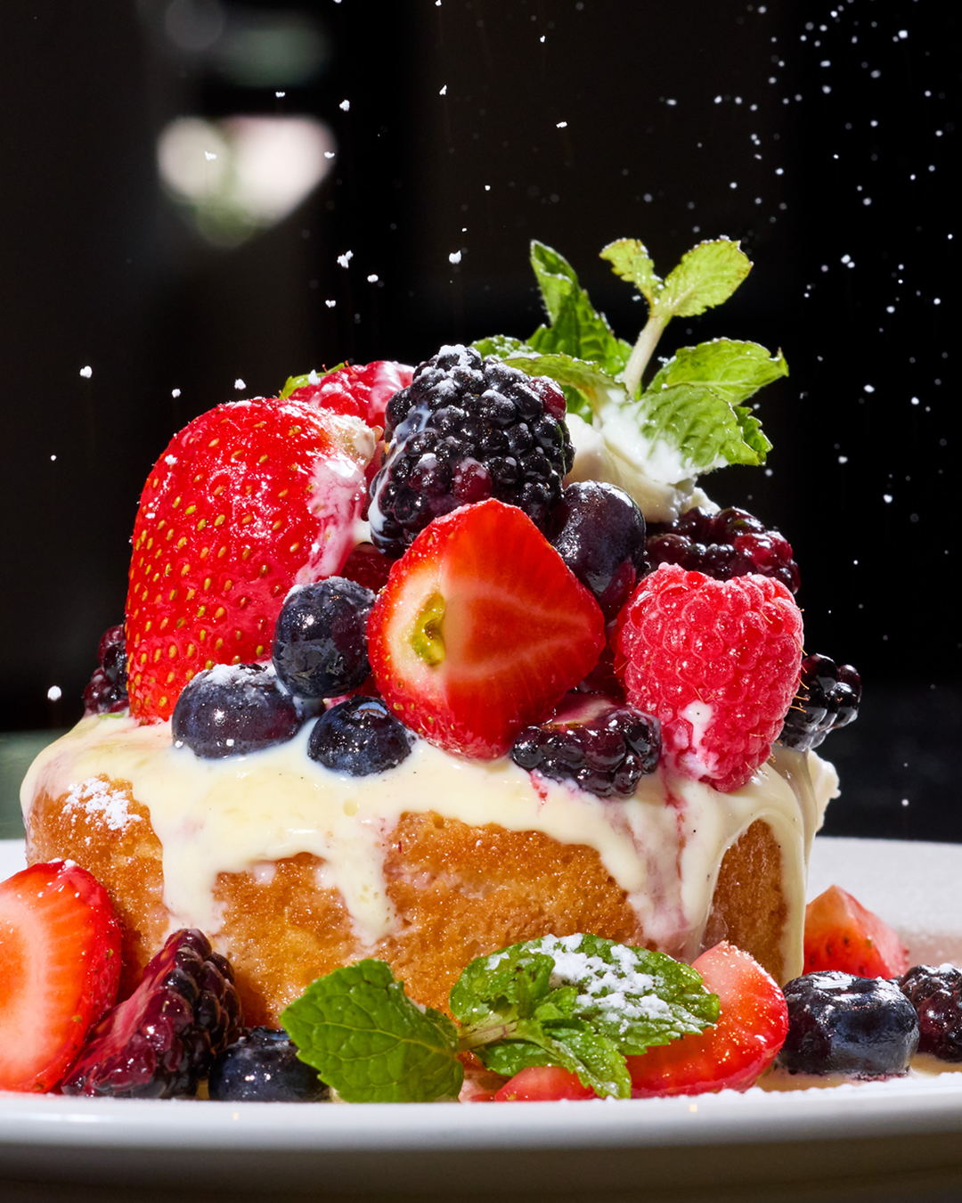 Seasonal mixed berry pound cake topped with strawberries, blueberries, raspberries, blackberries, cream, mint, and powdered sugar.