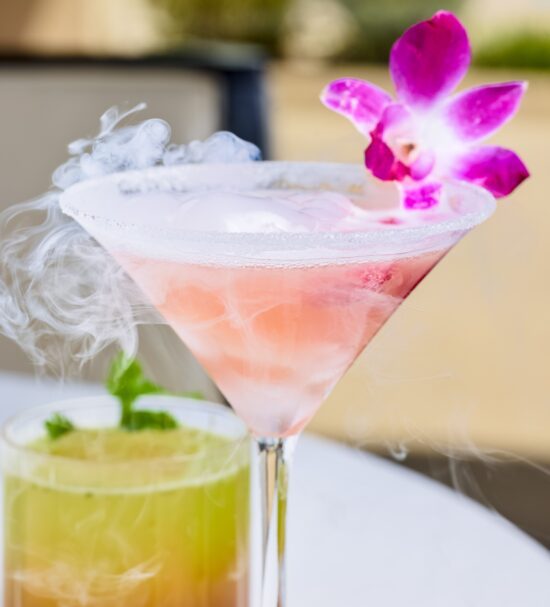 Voila! cocktail served in a frosted martini glass with smoking dry ice and a pruple orchid