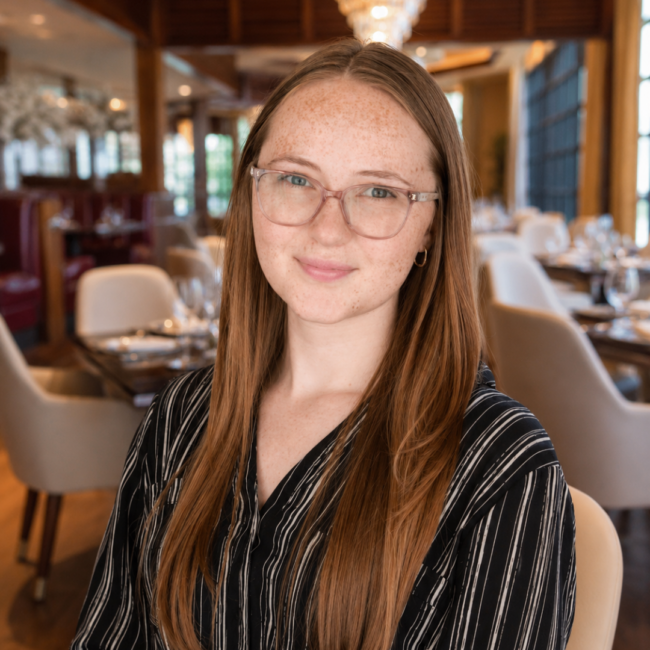 Sara Jamieson smiles for a professional headshot inside Truluck’s The Woodlands, with the elegant dining room softly blurred behind her.