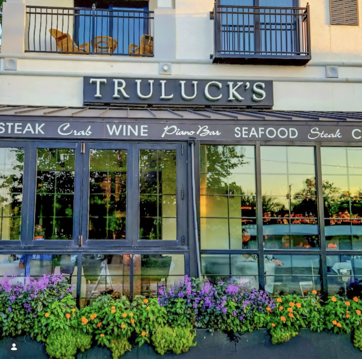Truluck's Naples exterior on Fifth Avenue South, awning reading Steak, Crab, Wine, Piano Bar, and Seafood above flower-lined windows at dusk.